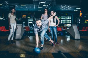 Friends playing bowling together. Man throwing ball while friends encurage him